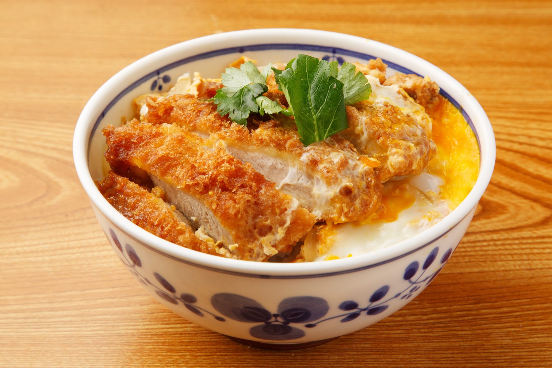A katsudon, a breaded pork cutlet with egg over rice, in a white bowl with a blue floral pattern on a wooden table