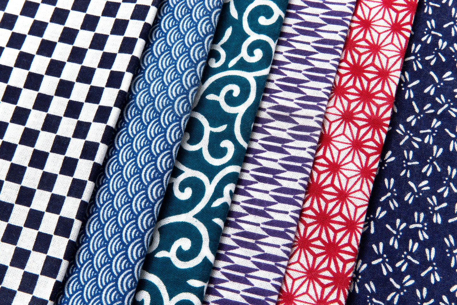 A row of folded Japanese cotton fabrics in different traditional patterns: checkerboard, waves, vines, and more