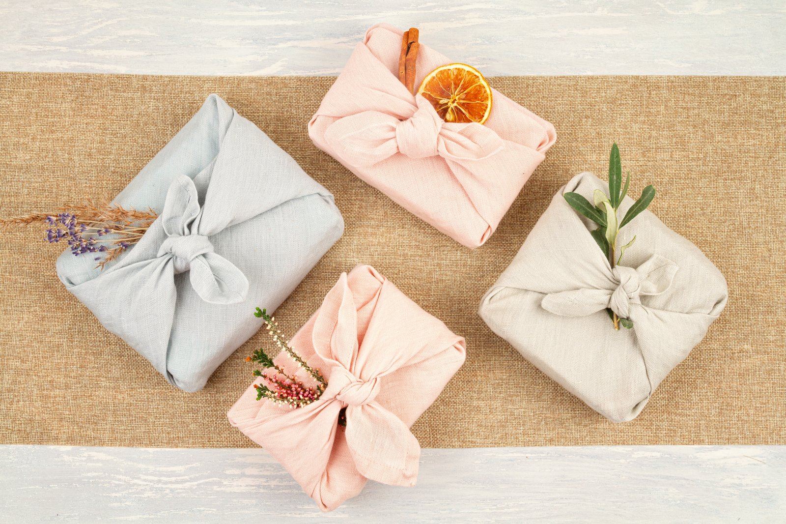 Four gifts wrapped in pastel-colored furoshiki cloth, tied with a knot and decorated with dried flowers