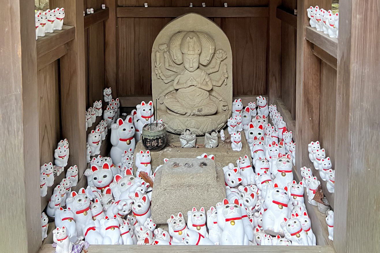 A small wooden shrine at Gotokuji with a stone Kannon statue surrounded by hundreds of small white cat figurines