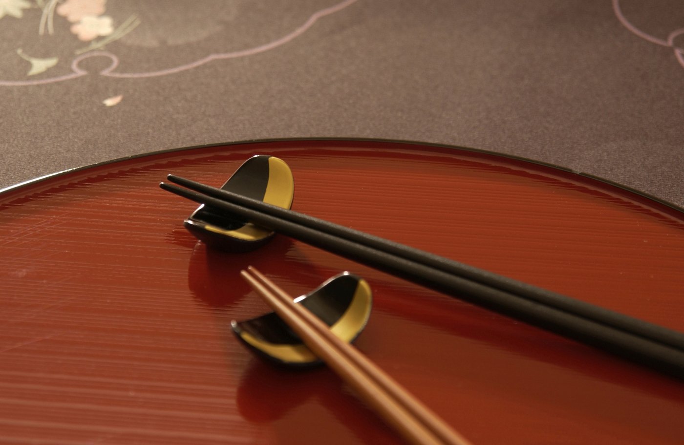 Two black and gold leaf-shaped chopstick rests holding chopsticks on a red lacquer plate