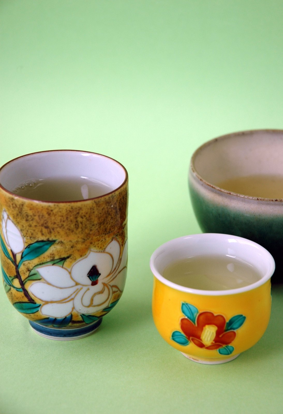 A Kutani ware yunomi teacup with a white magnolia and a small yellow cup with a red camellia, filled with green tea