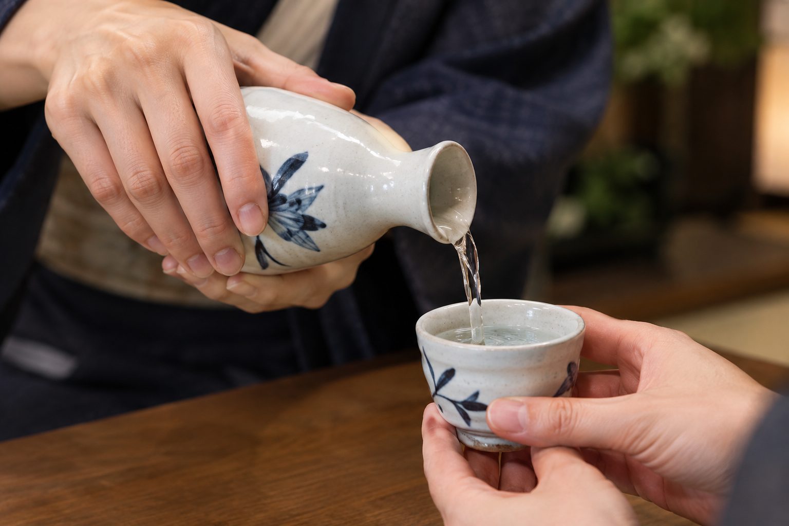 AI-generated image: Close-up of two hands pouring sake from a white and blue tokkuri into a small cup held up by another person